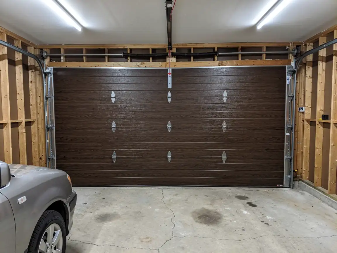 A brown garage door with decorative hardware is closed in a garage.